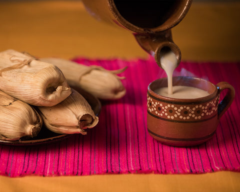 Taza de champurrado caliente en una mesa con 4 tamales.