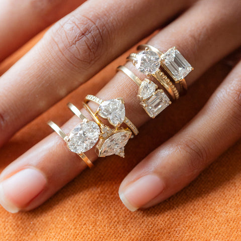 Model wearing six lab grown diamond engagement rings on with hand on brunt orange pillow