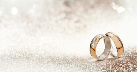 Two upright gold wedding bands symbolic of love and romance on a textured glitter background