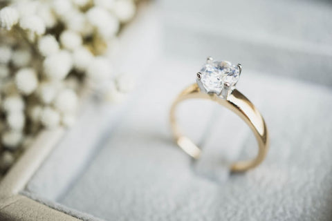 Diamond ring in box with white flower background.