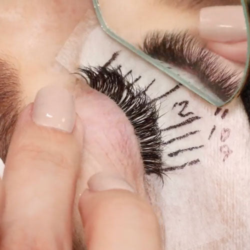 A photo showing a completed set of hybrid lashes. The client's eye is closed and the technician is using a lash mirror to check the lashes from underneath | London Lash Canada