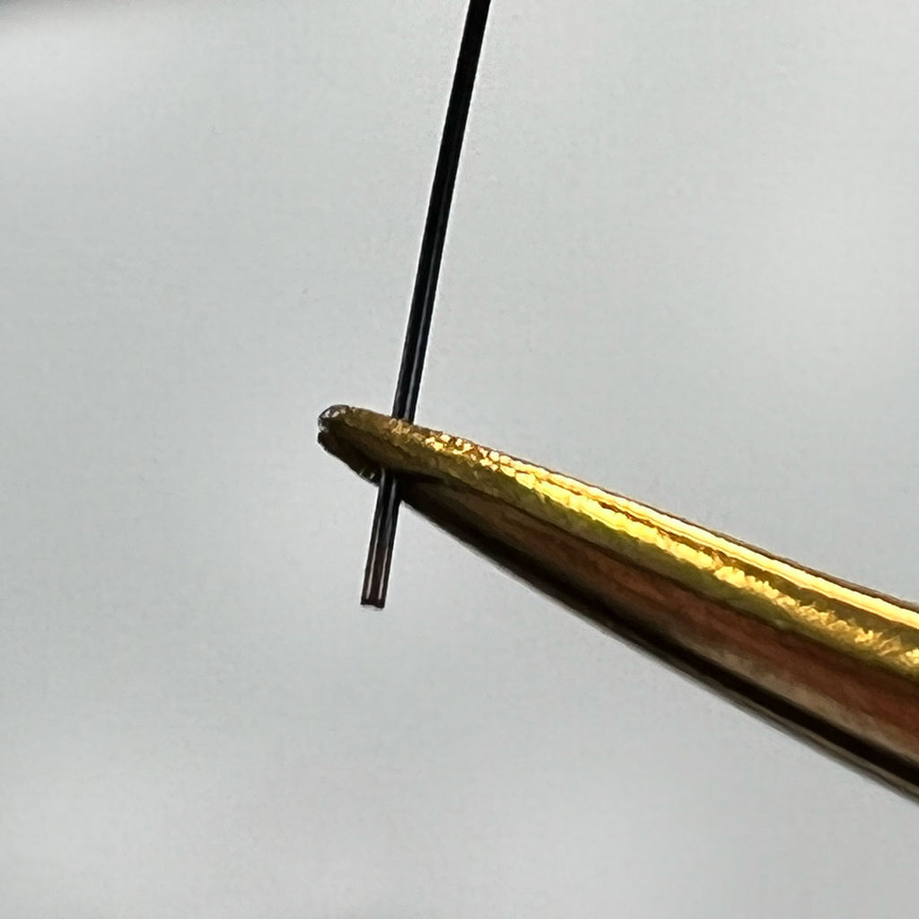 an extreme close up of a flat lash held in a pair of lash tweezers to show the shape of the base