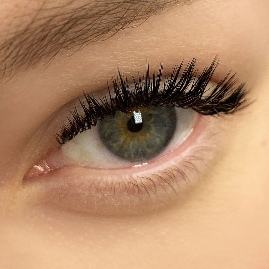 a close up of a set of wet look lashes on a grey and green eye.