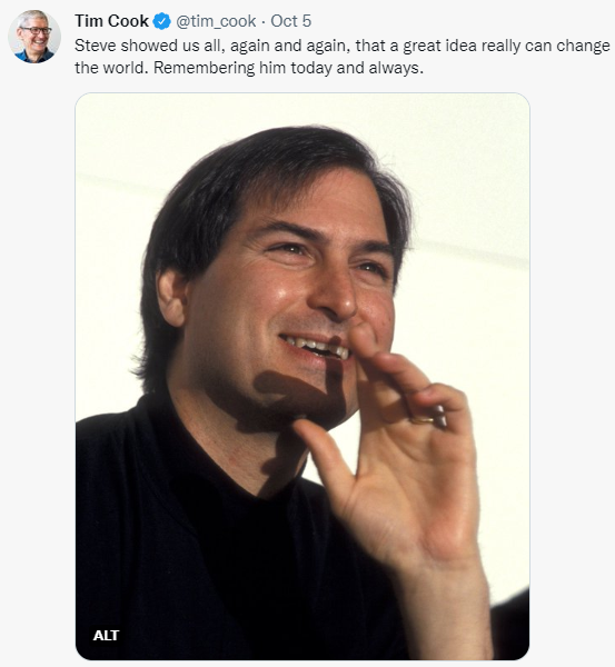 Steve Jobs, in his signature black turtle neck, smiling and gesturing with one hand.