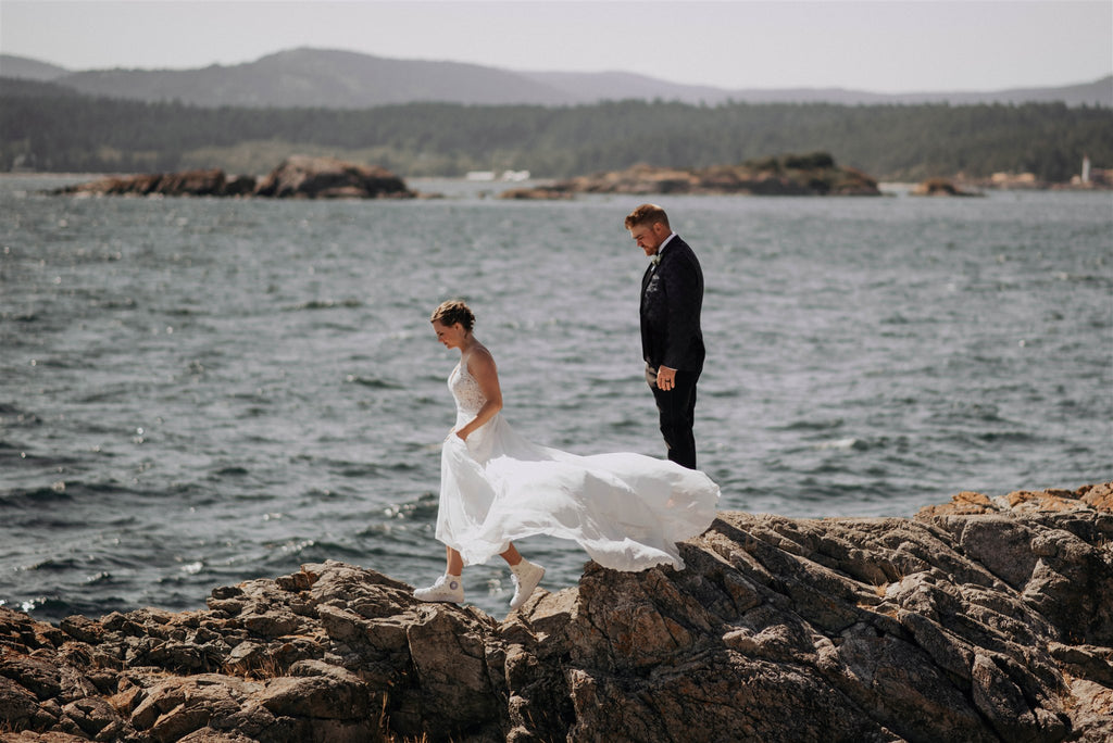 Bride and groom climbing over rocks next to the ocean