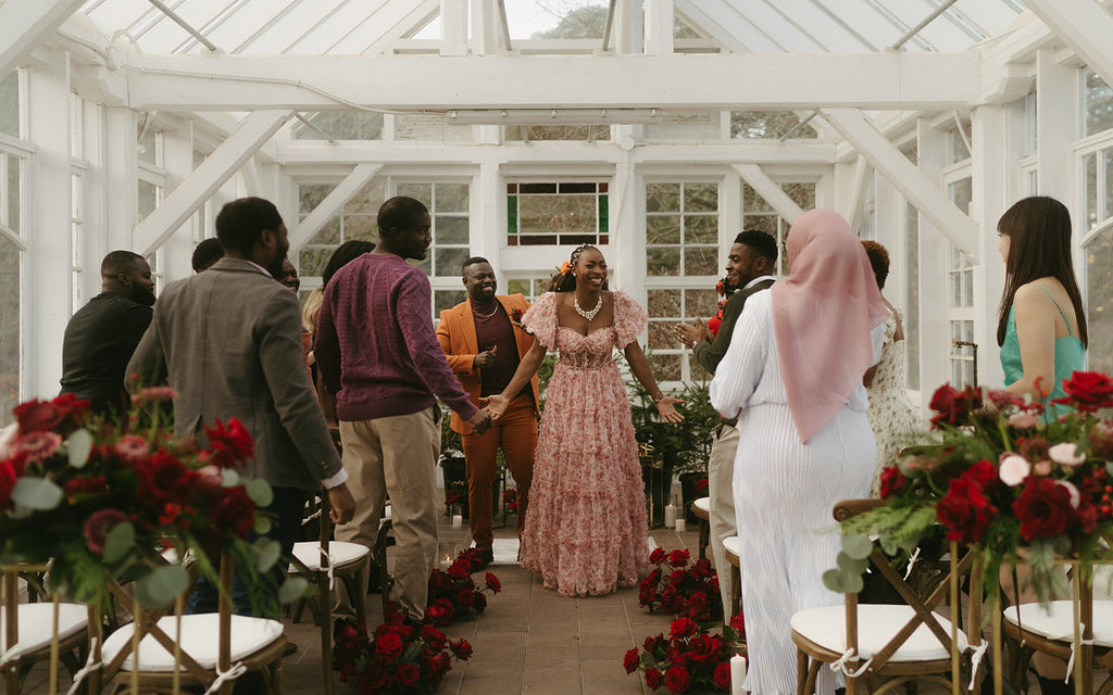 Bride and groom in colourful wedding suit and dress celebrating at the end of their ceremony with guests in a glass green house.