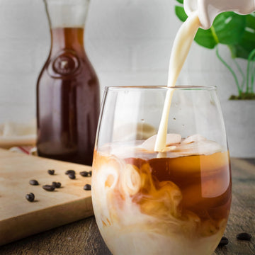 cream being poured into a glass of cold brew coffee