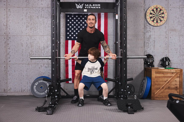 A father teaching his son weightlifting using a Smith machine in a home gym.