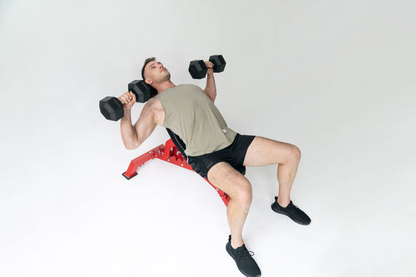 A man performs a dumbbell bench press on an inclined bench