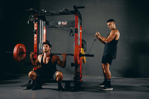 a man doing squat and other one doing biceps curl on same power rack at the same time