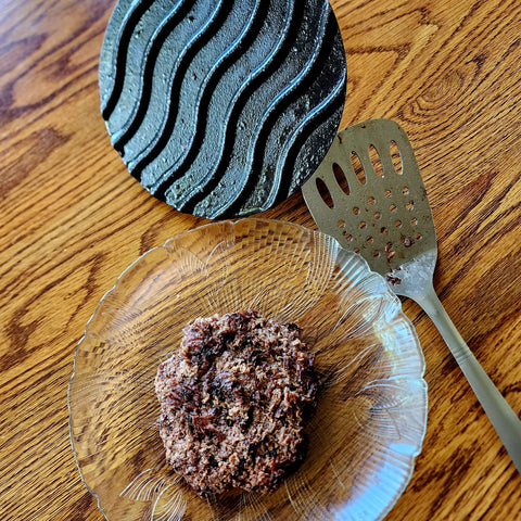 Smash burger on a plate beside a spatula and a cast iron hamburger press.