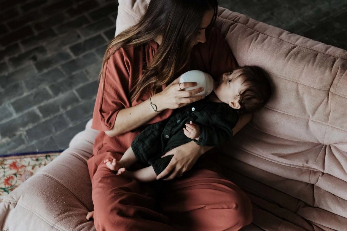 Bébé dans les bras de sa maman qui boit son biberon physiologique Elhee