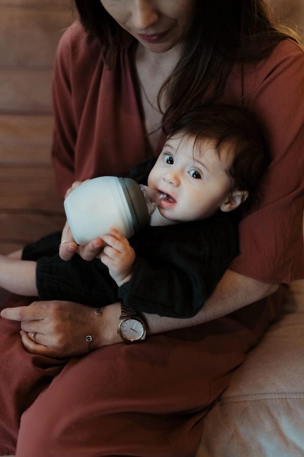 Bébé dans les bras de sa maman qui tire sur la tétine physiologique de son biberon anti-colique Élhée