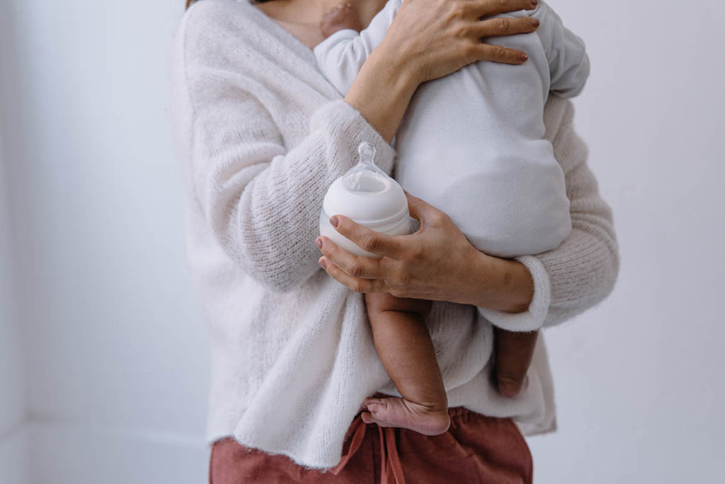 eine Mutter mit einem Baby im Arm und einer Flasche Elhee