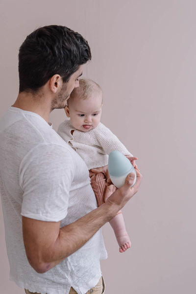 ein Vater hält sein Baby und eine Flasche Elhee im Arm