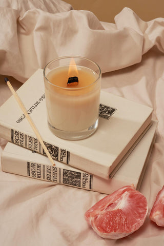 scented burning candle set on top of books on white cotton bedsheets.  Peeled grapefruit lies beside the candle.