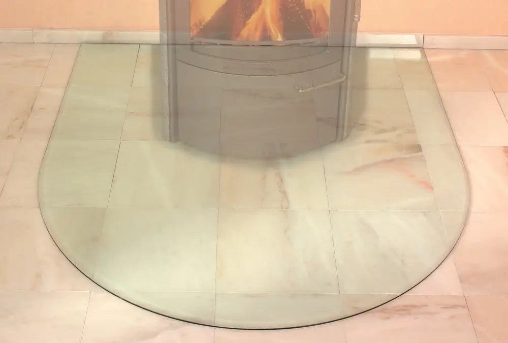 Beispiel einer gebogenen Funkenschutzplatte aus Glas auf einem hellen Fliesenboden unter einem Kaminofen - ofenerlebnis.de