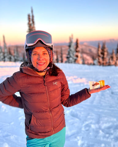 Jess holding a Salted Chai with Chia Bar during a golden hour ski sesh.