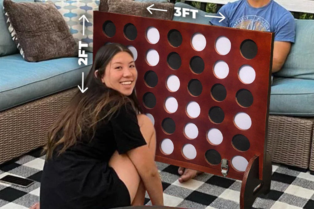 Woman sitting next to Giant Four-in-a-Row tailgate game with dimensions of the game shown