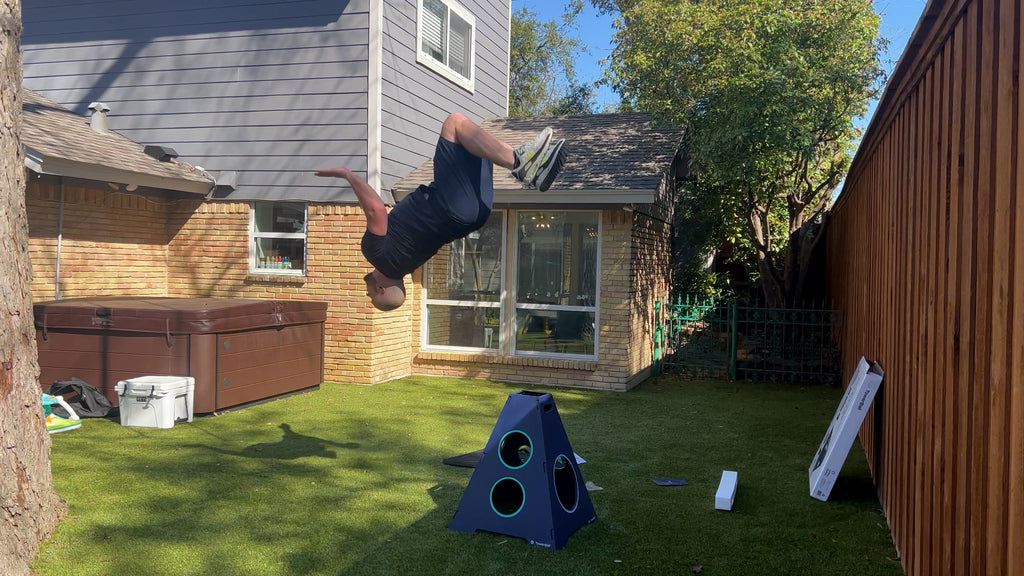 Man in backyard does backflip over TowerBall tower.