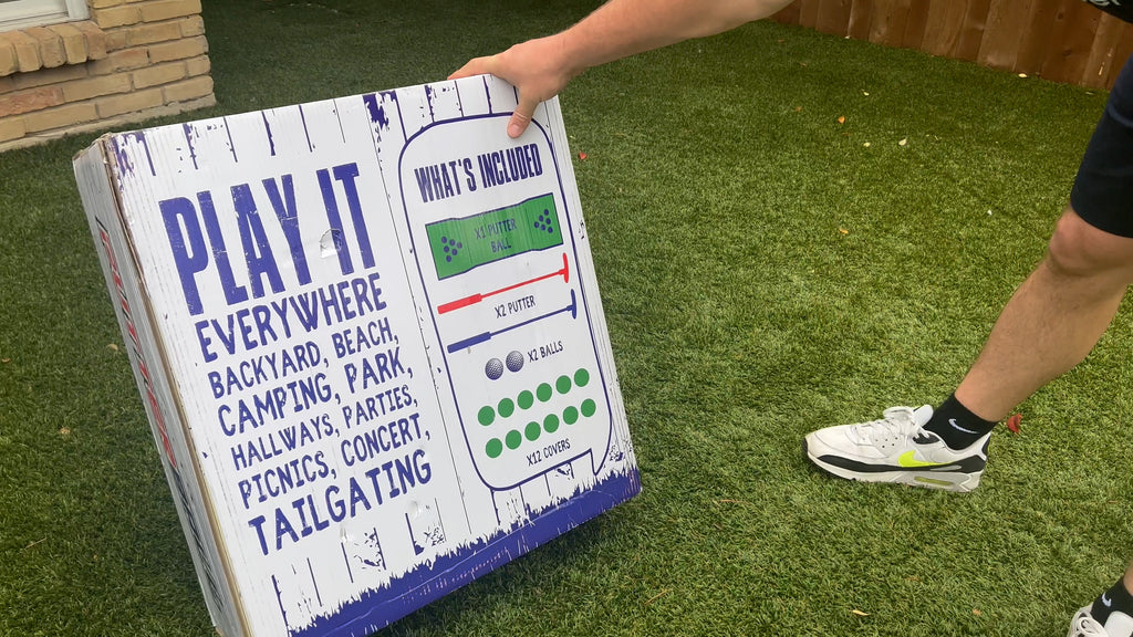 Man stands in backyard holding Putterball box.