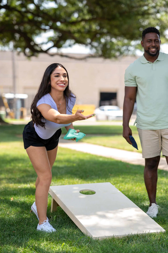 Women smiling as she throws a bean bag towards the cornhole board