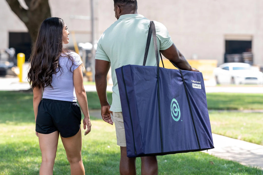 Man carrying cornhole game in its storage bag walking and talking with woman by his side