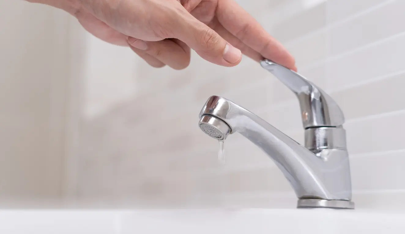 Hand turning off a chrome faucet with a single water droplet forming.