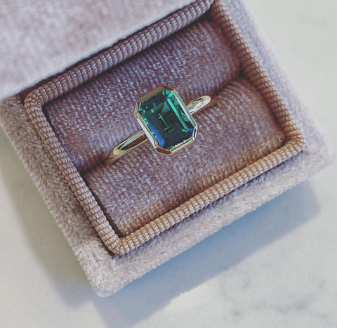 an emerald cut emerald is bezel set into yellow gold