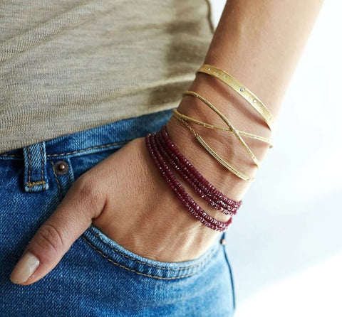 a woman wearing a ruby wrap bracelet alongside yellow gold bracelets