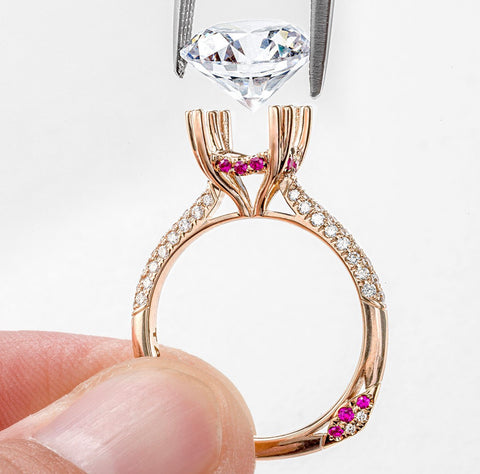a diamond is being set into a rose gold engagment ring with accent pink sapphires