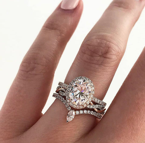 An oval halo engagement ring stacked with two different diamond wedding bands