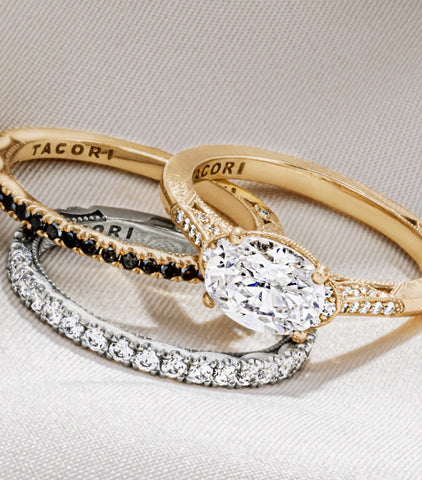 a oval cut diamond is set east-west on a yellow gold band and shown with a black diamond band and a white gold diamond band