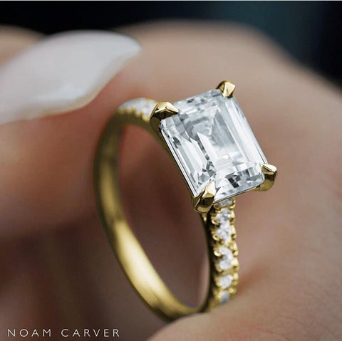 an emerald cut diamond is set east-west on a yellow gold diamond band