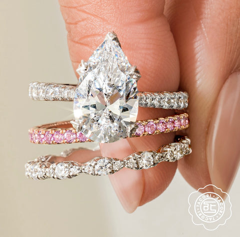 a pear cut diamond engagement ring is accompanied by a pink sapphire & white diamond bands