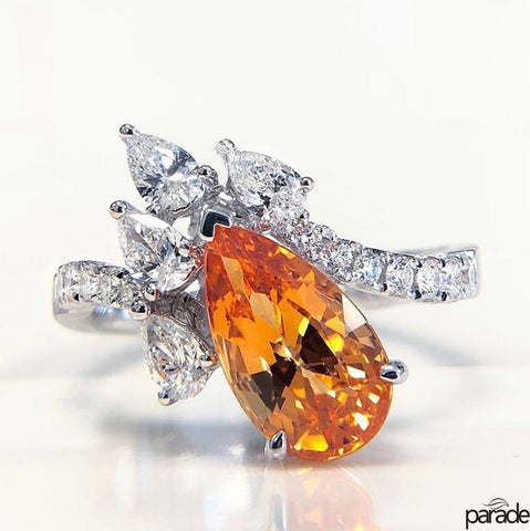 a pear shaped spessartite is on a white gold ring accented but marquise and round brilliant cut white diamonds