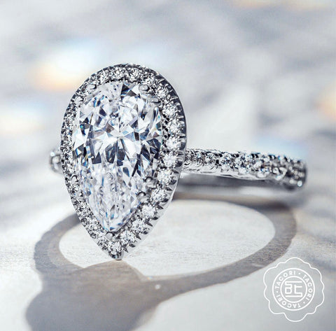 a pear shaped diamond is set with a halo and diamond band