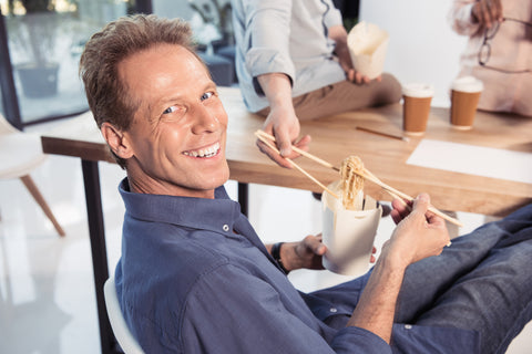 Man smiling and eating using the chopsticks