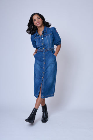 A lady wearing a blue denim midi dress with a gold Scamp & Dude button front and plait detail on the chest and waist