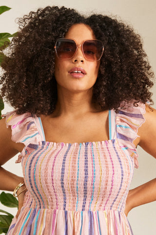 A curly-haired lady wearing blush pink oversized '70s style sunglasses with smoke to pink gradient lenses