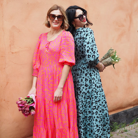 Emma Paton and Claudia Beresford holding flowers, wearing Scamp & Dude Tie Front Maxi Dresses and sunglasses 