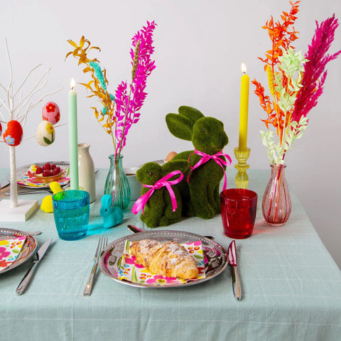 An Easter themed tablescape with bright flowers, candles and glasses, bunny ornaments and an almond croissant