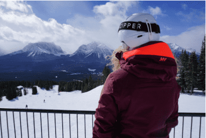 Woman in ski helmet and ski jacket looking at snowy mountains from a balcony