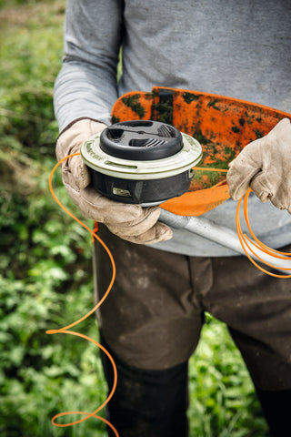 Homme qui recharge du fil dans la tete de sa débrousailleuse