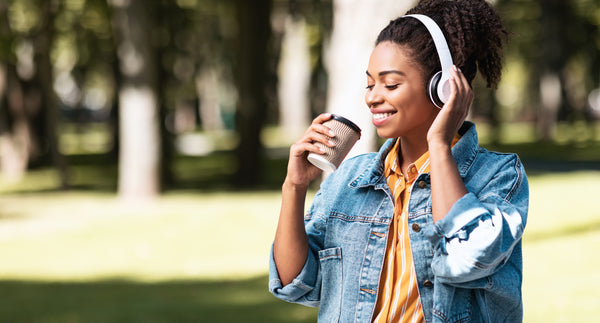 Weekend Concept. African Millennial Girl With Headphones Having Coffee Enjoying Day Walking Outside In Park. Panorama, Copy Space