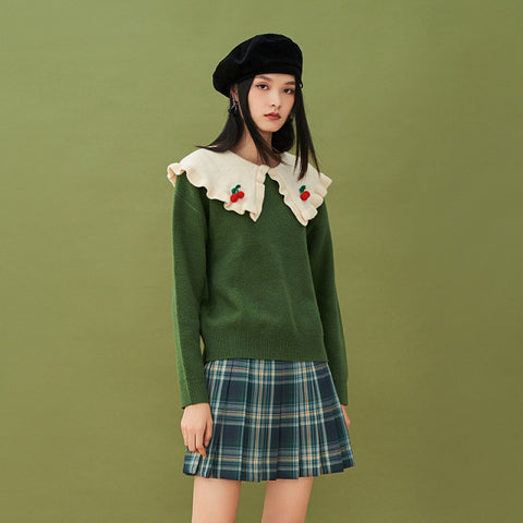 A girl wearing green sweater and pleated skirt