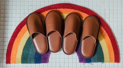 Des chaussons marrons sur un tapis arc en ciel, avec un fond en carrelage blanc