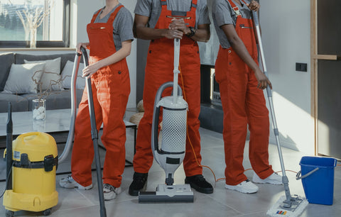 Trois personnes en tenue orange qui font le ménage avec un aspirateur, un balai vapeur et une serpillière