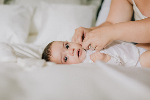 Baby Lays On White Duvet Looking At The Camera