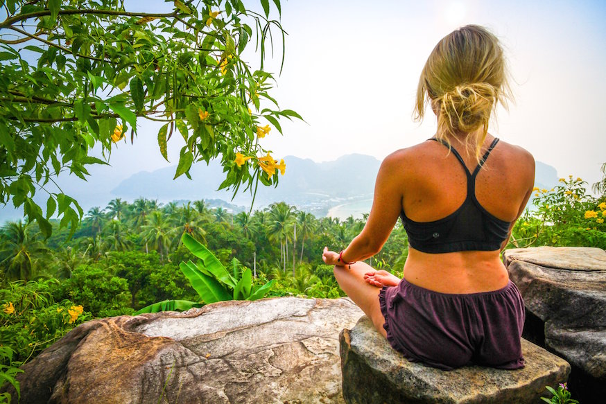 Girl sitting on a stone in the lotus position looking into the distance somewhere deep in the jungle